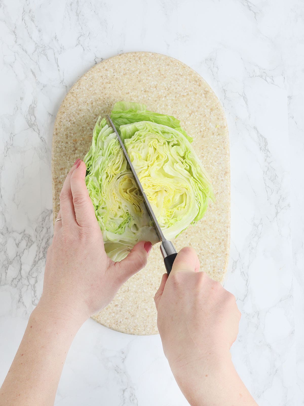 pair of hands using a sharp knife to cut a head of iceberg lettuce into quarters