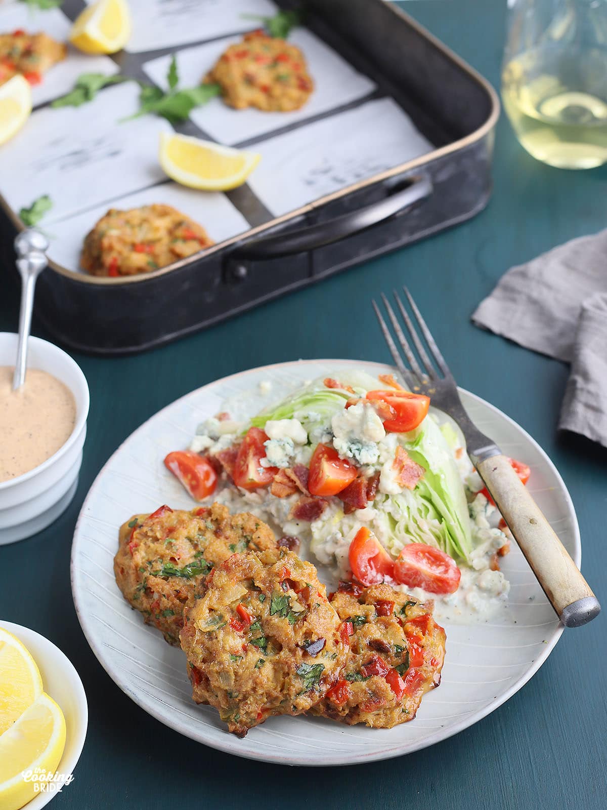 three oven baked crab cakes on a plate with a salad to the side and a tray of crab cakes in the background