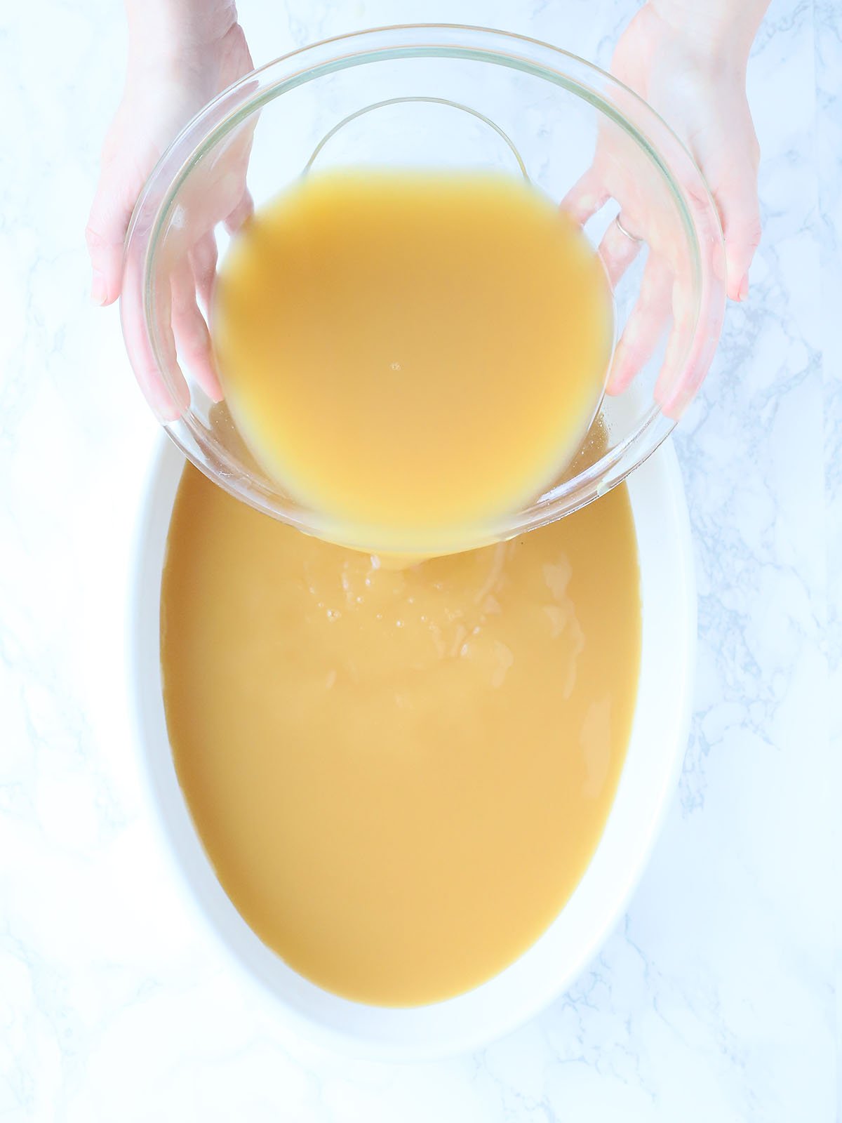 pair of hands pouring the unfrozen slush mixture into a large dish for freezing
