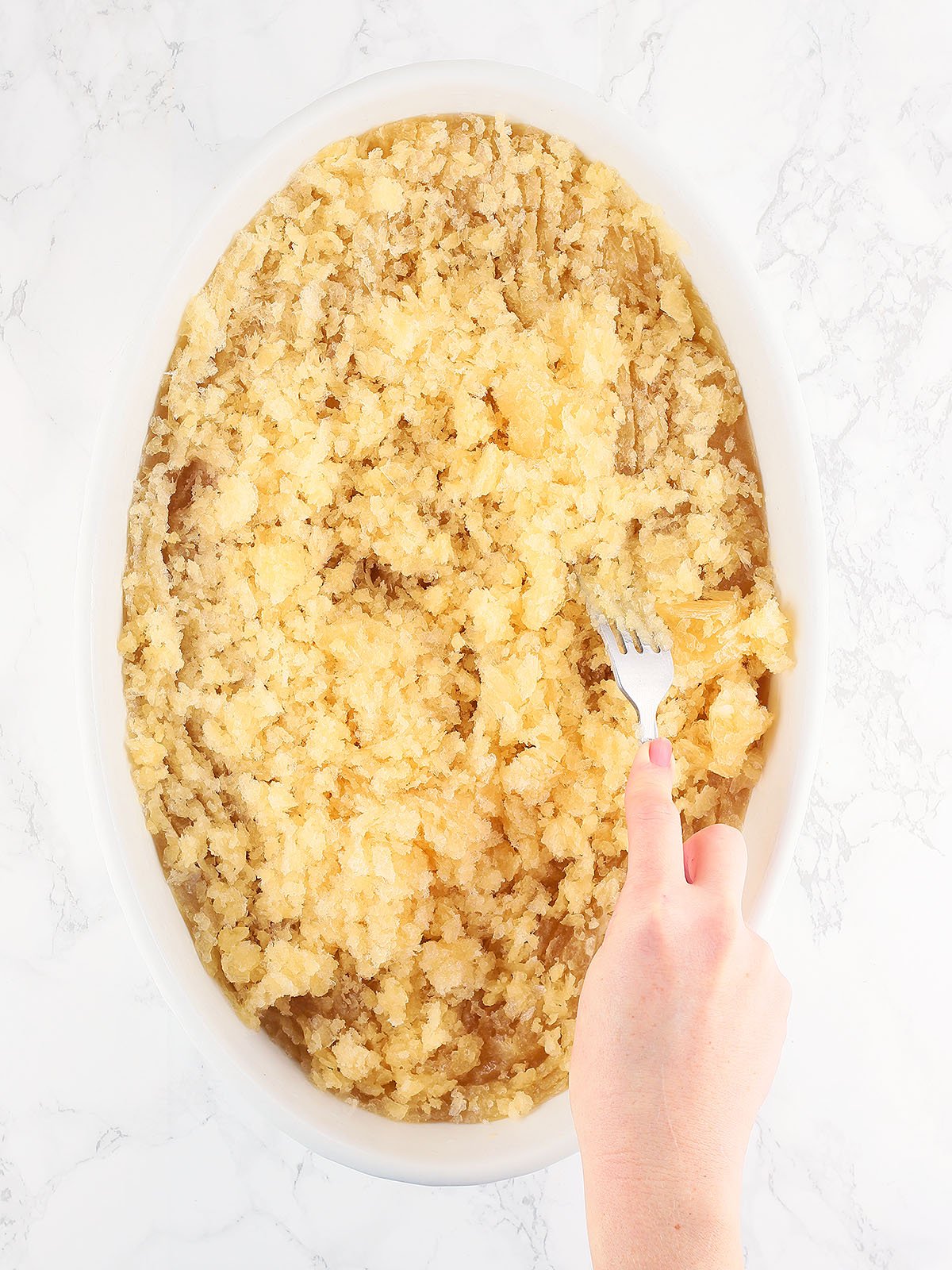 hand using a fork to scrape the frozen mixture