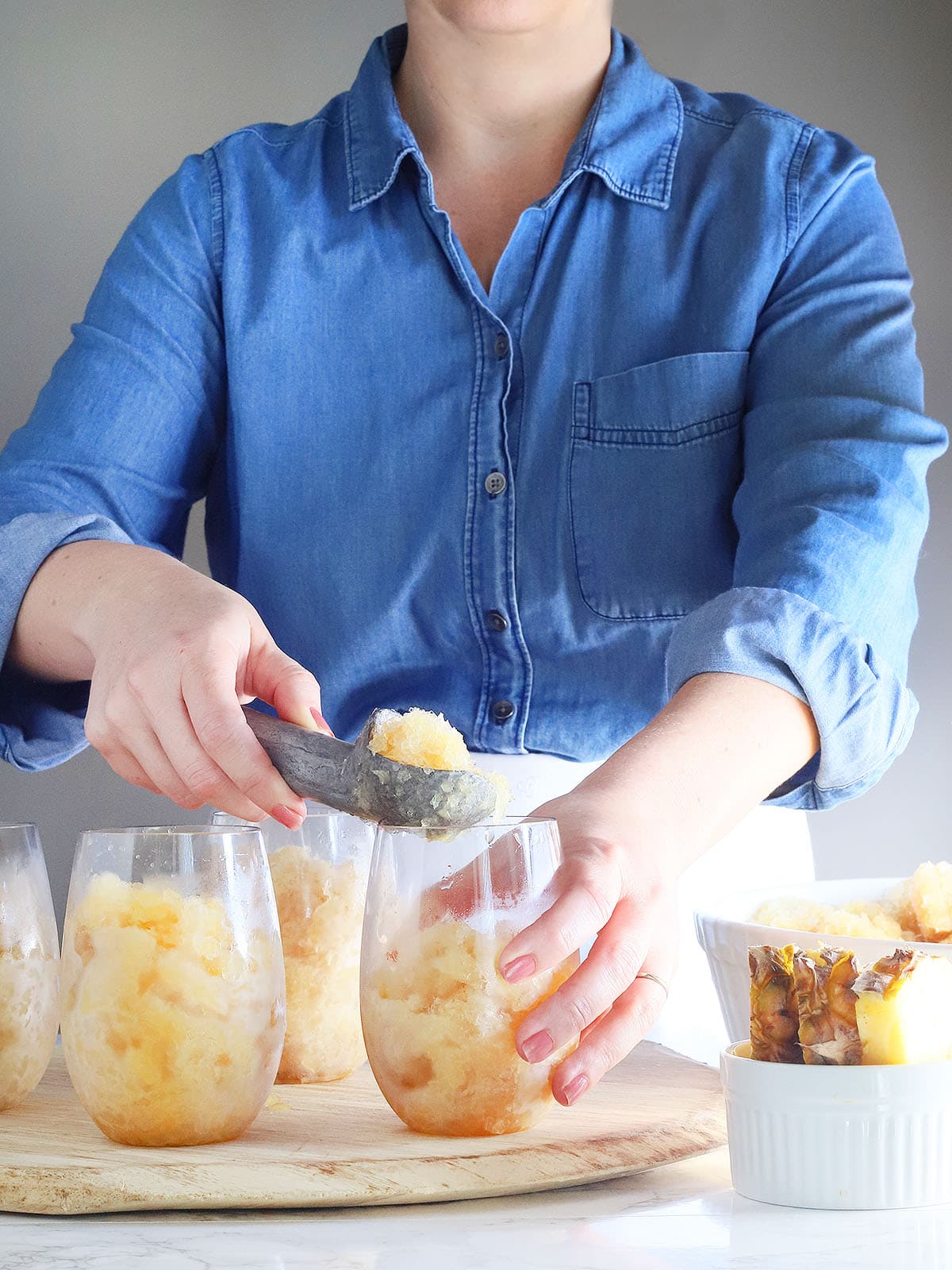 woman using a metal ice cream scoop to serve bourbon slush into clear glasses