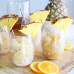 four glasses of bourbon slush garnished with pineapple wedges arranged on a round wooden tray