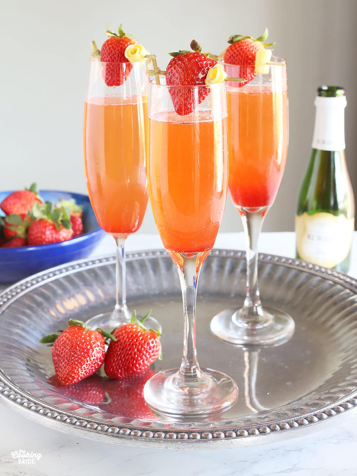 three filled champagne flutes garnished with strawberries on a silver tray
