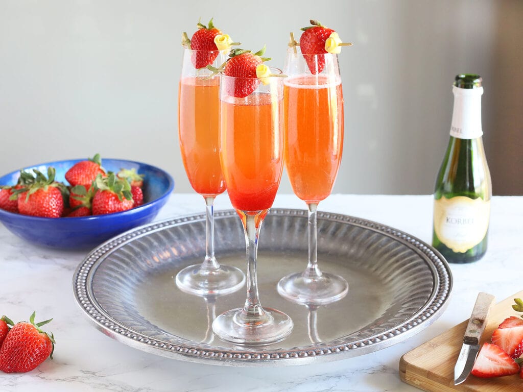 three strawberry champagne cocktails sitting on a silver tray