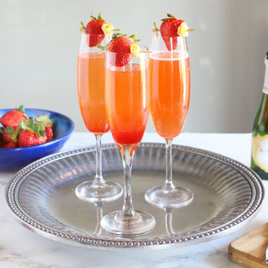 three strawberry champagne cocktails sitting on a silver tray