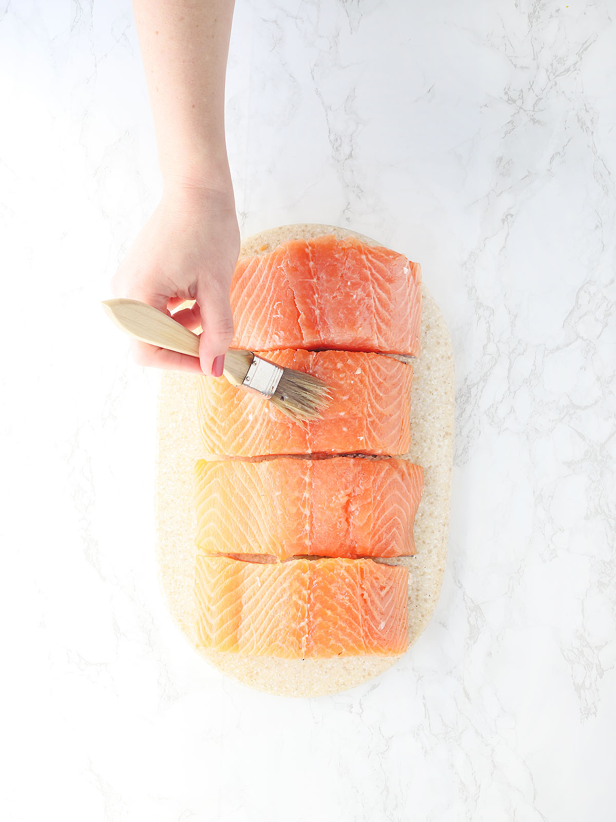 hand brushing four salmon fillets with olive oil