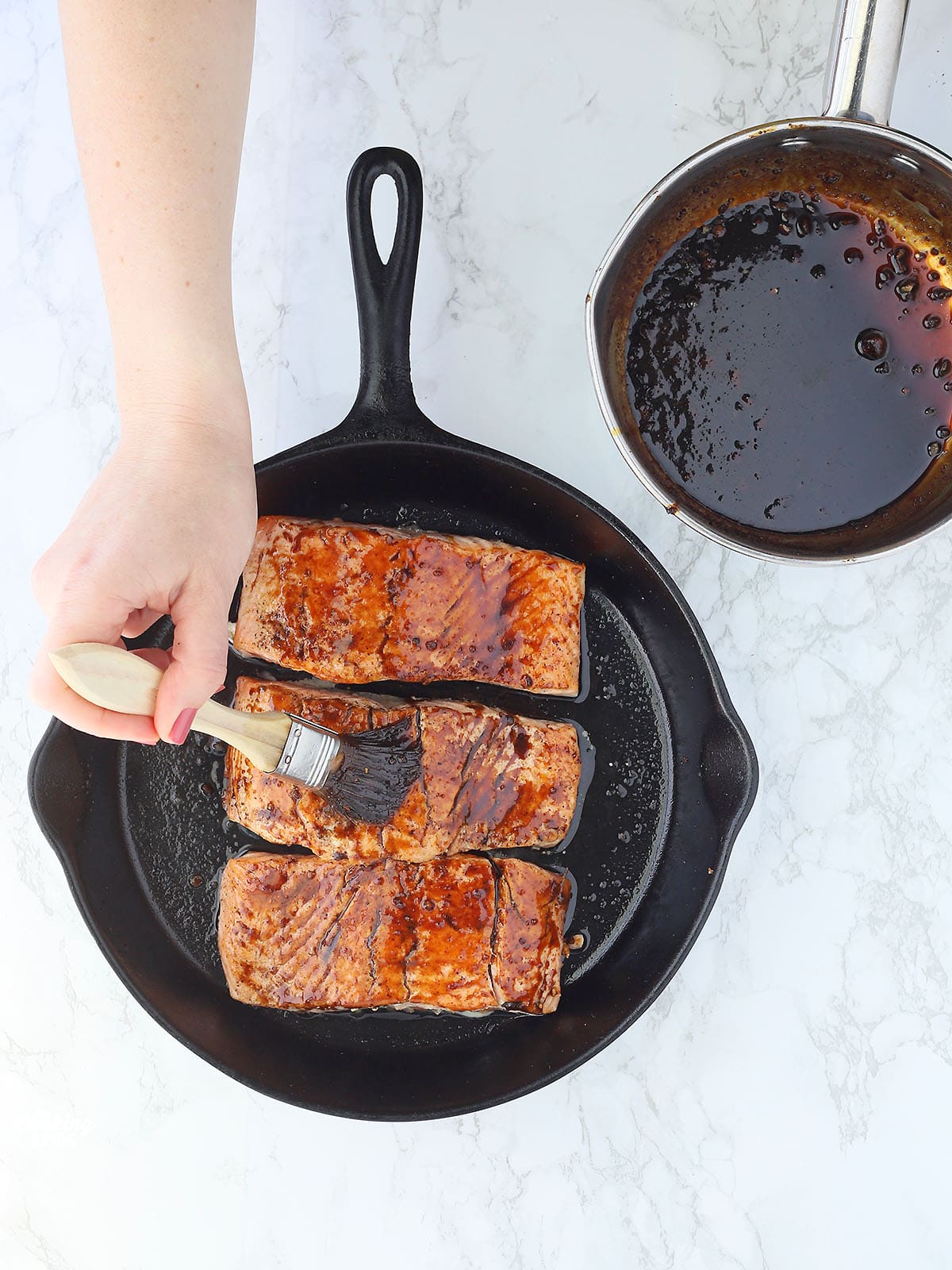 hand brushing molasses glaze over salmon filets in a cast iron skillet