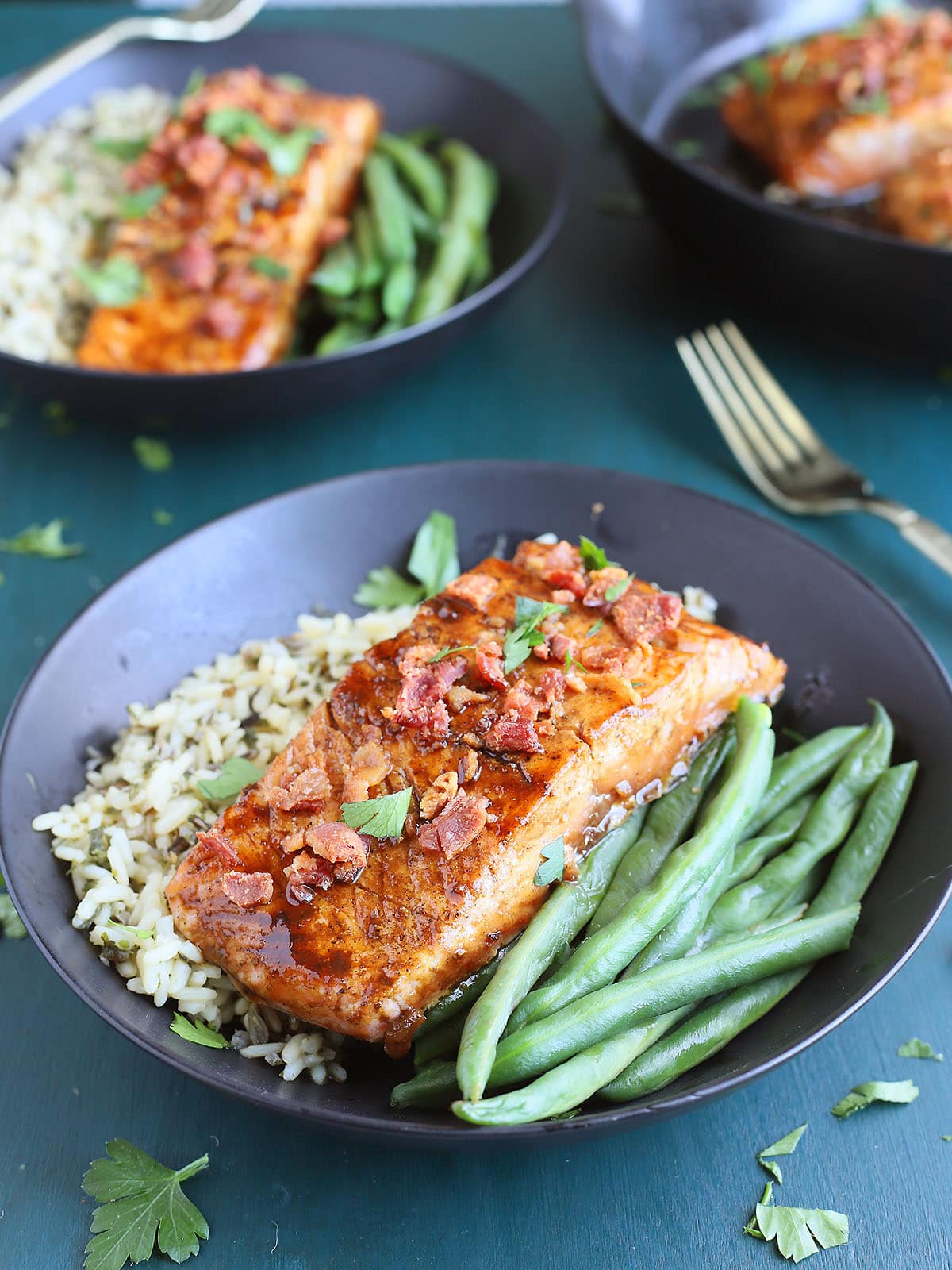 a glazed salmon filet on a bed of rice and fresh green beans in a black bowl