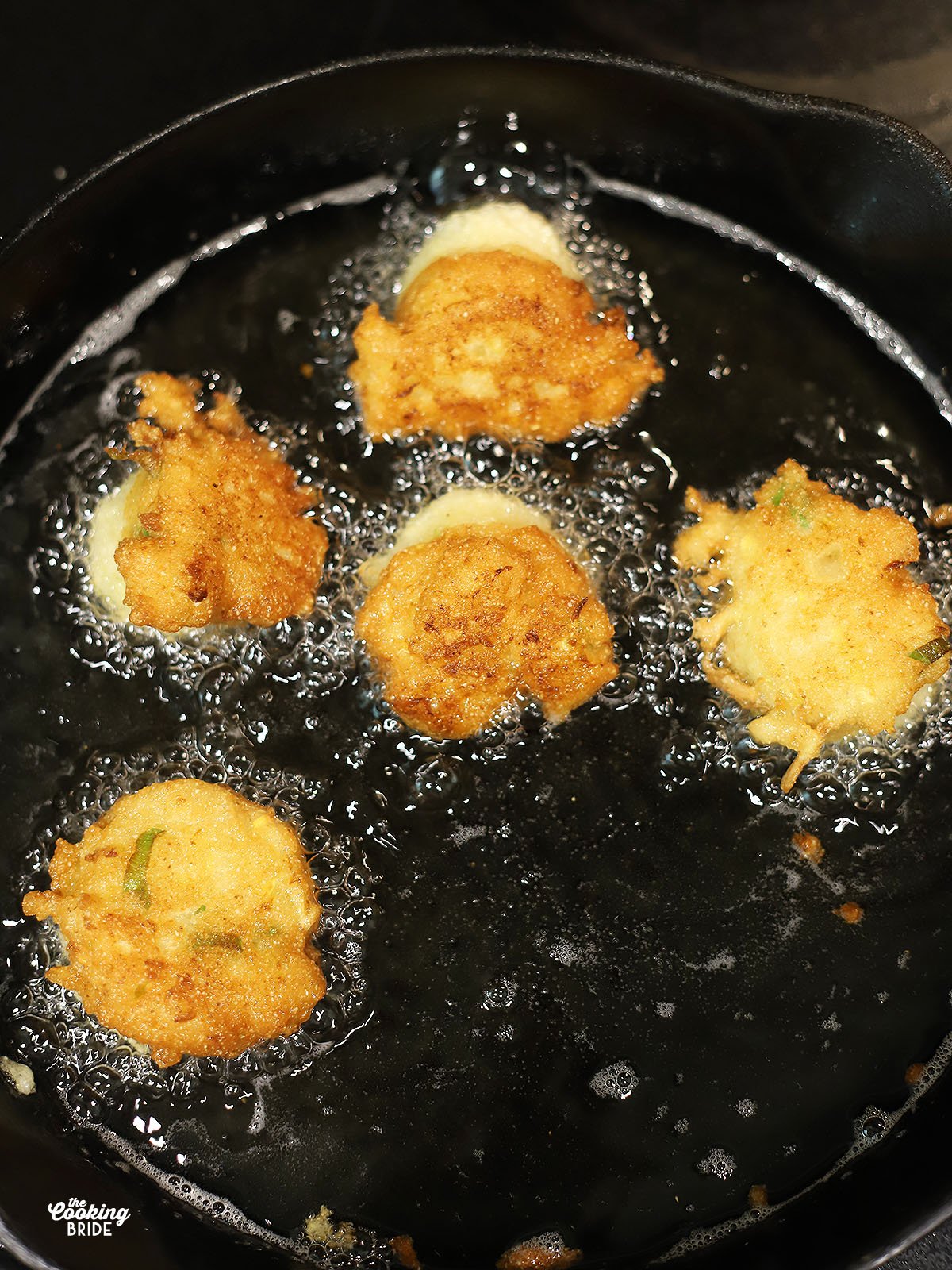 squash puppies frying in oil in a cast iron skillet