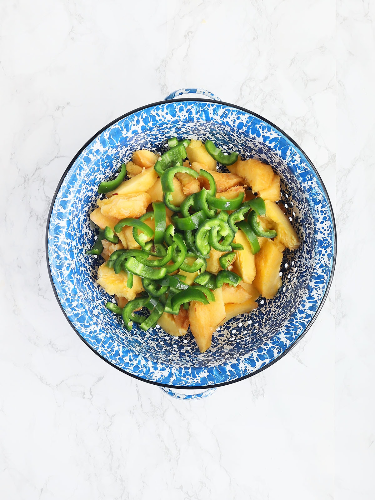 Sliced peaches and jalapeno peppers in a blue and white colander.