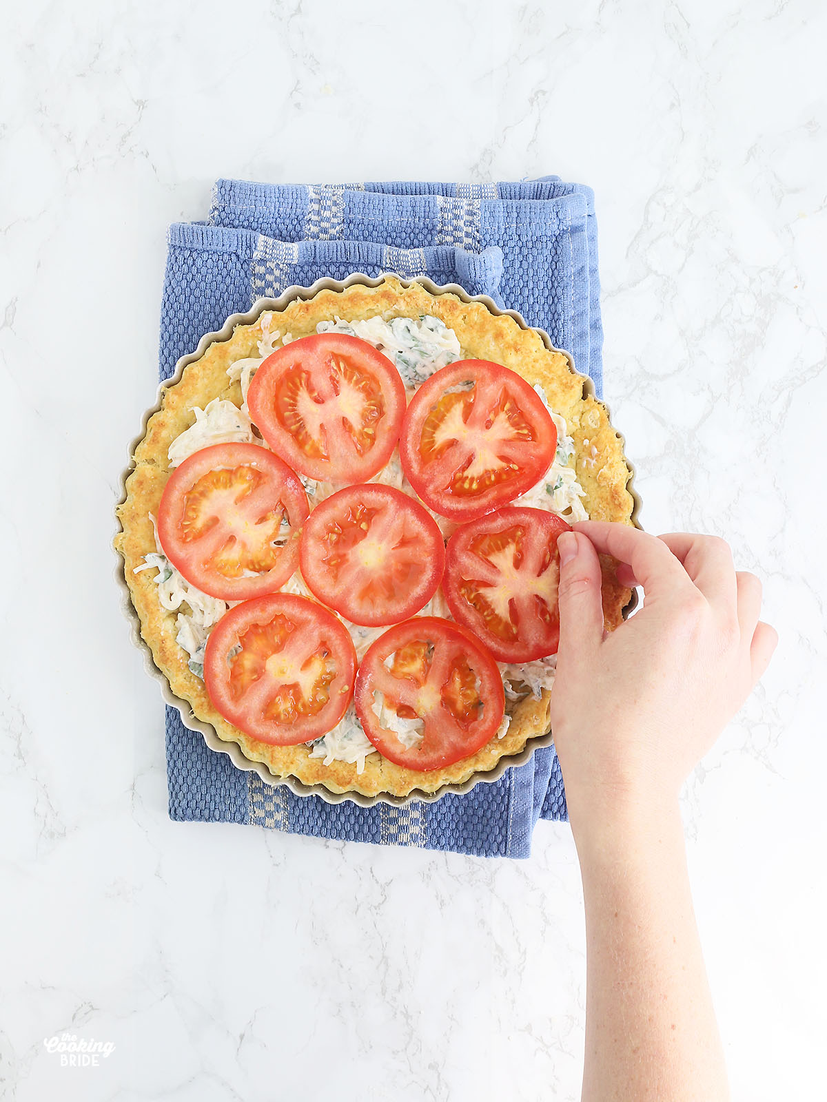 hand placing sliced tomatoes on top of a southern tomato pie