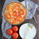 baked southern tomato pie on a dark wooden table with fresh tomatoes, plates and forks to the side