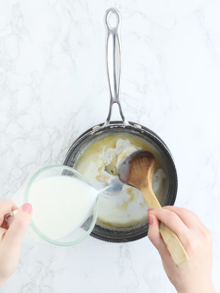 hand pouring cream into a saucepan with butter and flour