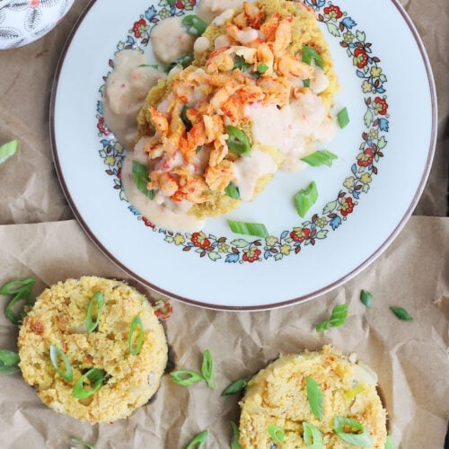crawfish cornbread cut into rounds on a brown paper lined baking sheet, a small pitcher of gravy and a plate of cornbread covered in gravy and crawfish tails to the side