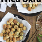 overhead shot of two black dishes filled with fried okra, a black and white napkin, metal strainer and whole okra to the side