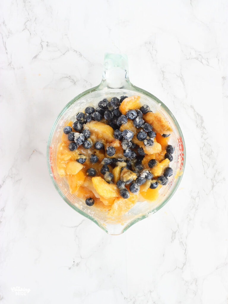 blueberries and peaches mixed with sugar in a large mixing bowl