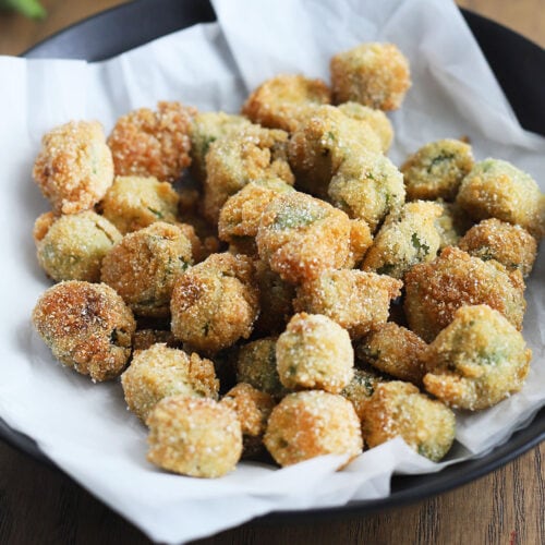 Black dish of fried okra on a wooden background.