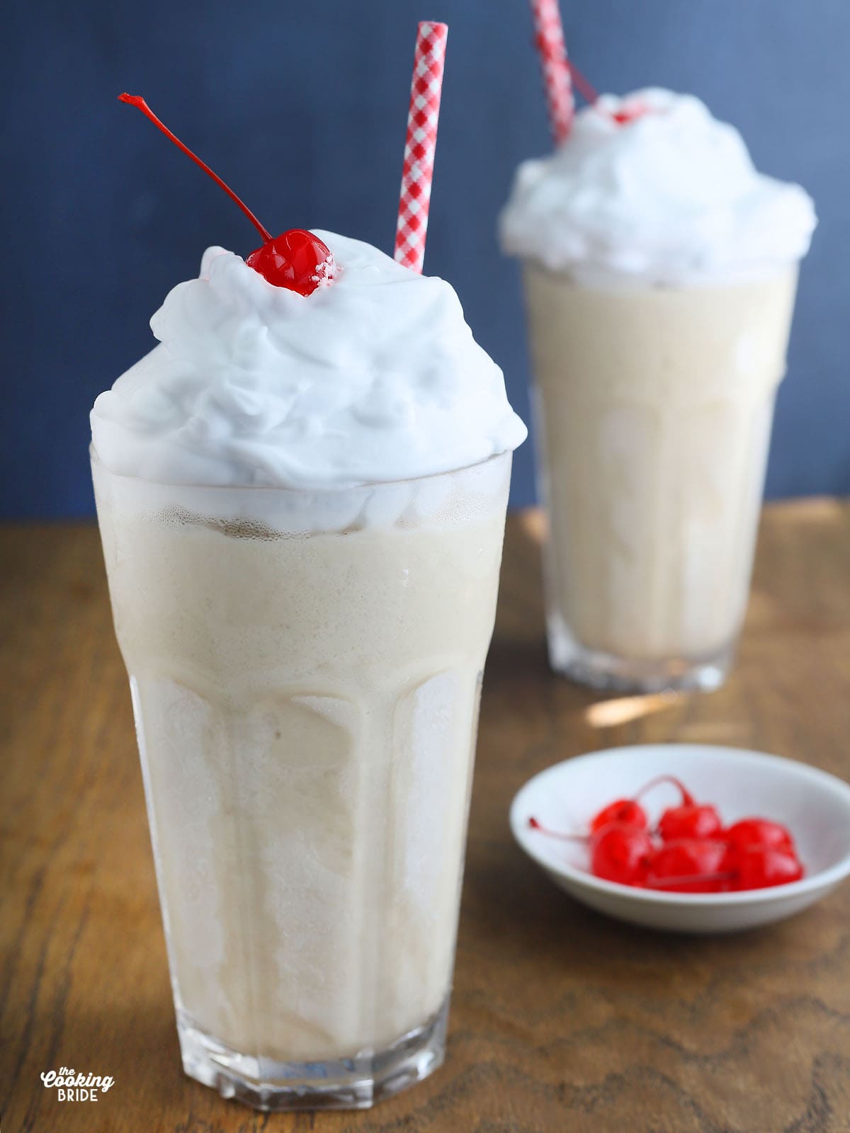 two frozen bushwacker cocktails with whipped cream, cherries and a red and white straw. Small dish of cherries to the side.