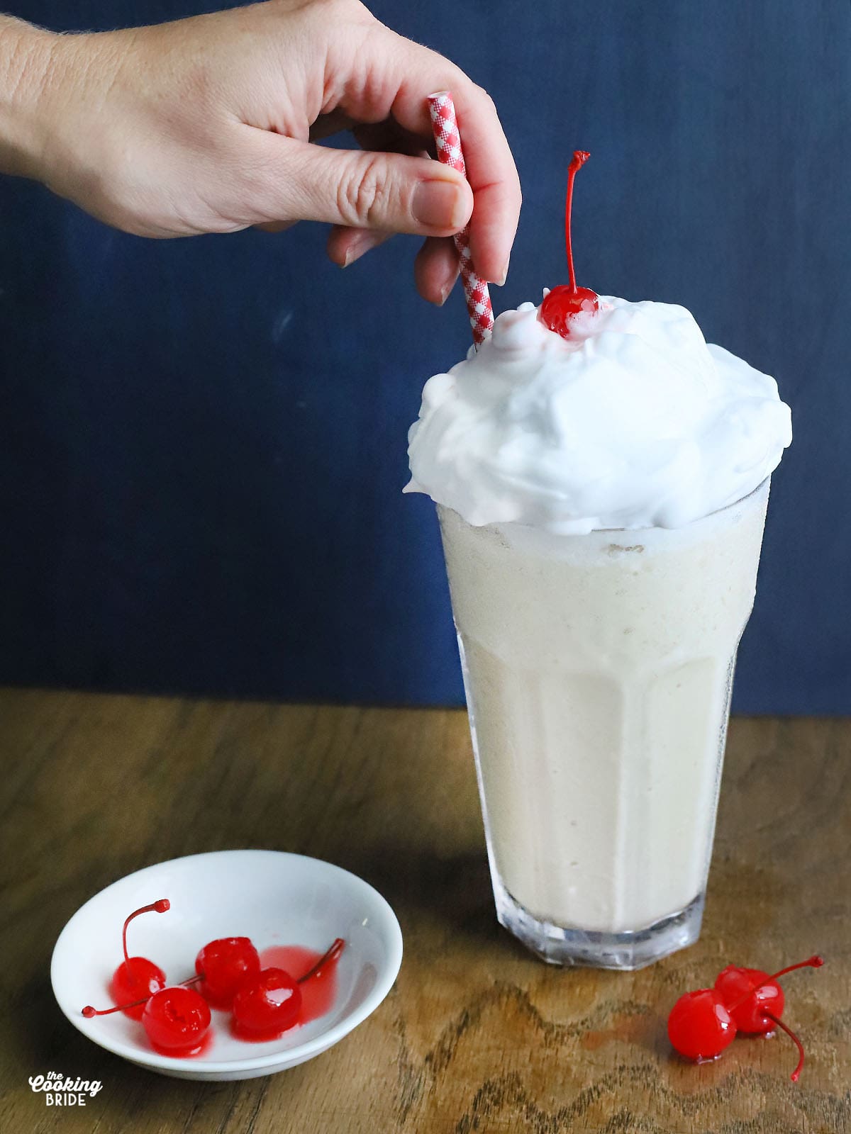 hand placing a red and white straw into a frozen bushwacker cocktail topped with whipped cream and a cherry