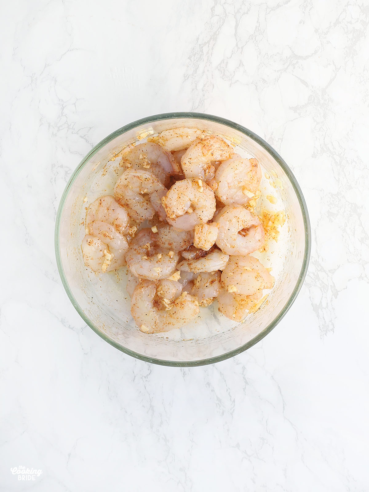 shrimp seasoned with olive oil, minced garlic and Cajun seasoning in a glass bowl
