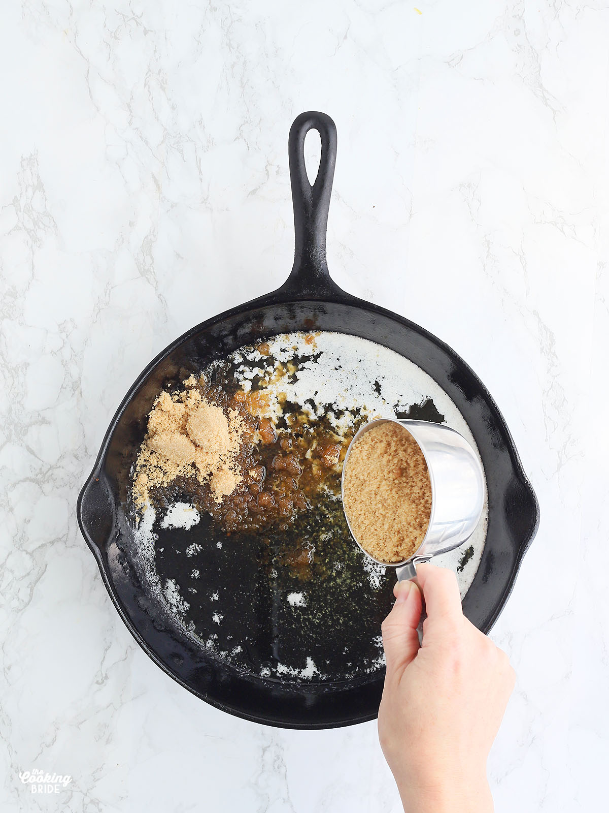 hand sprinkling brown sugar into melted butter in a cast iron skillet