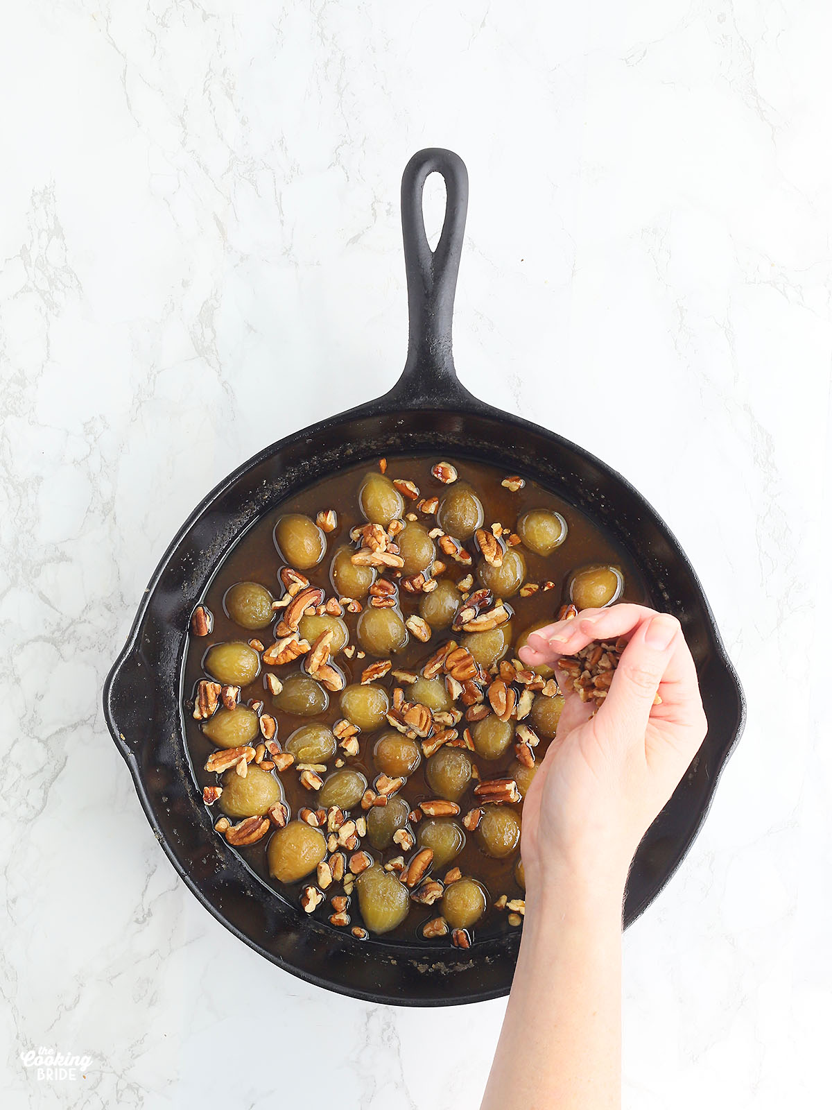 hand sprinkling chopped pecans over the figs in a cast iron skillet