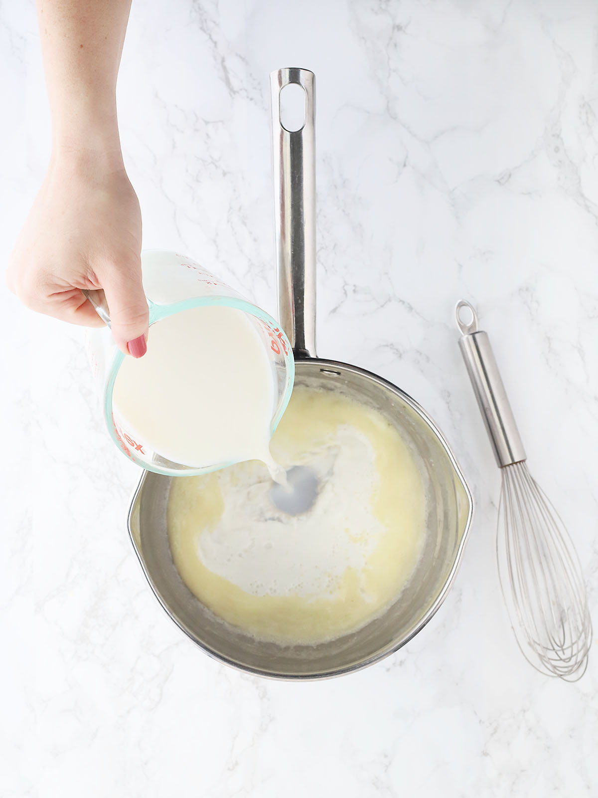 hand pouring milk into a saucepan with melted butter and flour