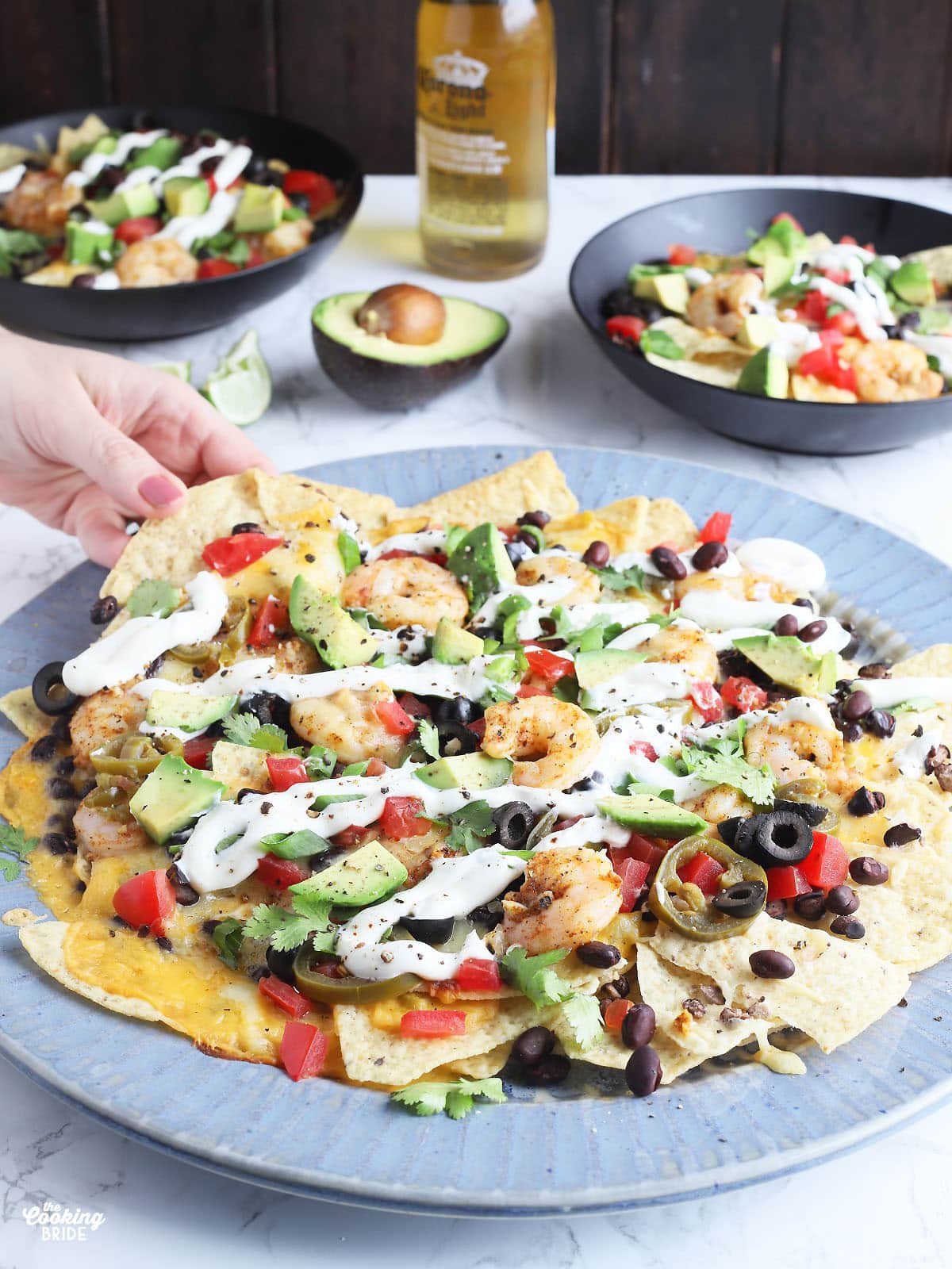 hand reaching for a chip from a large blue platter of shrimp nachos