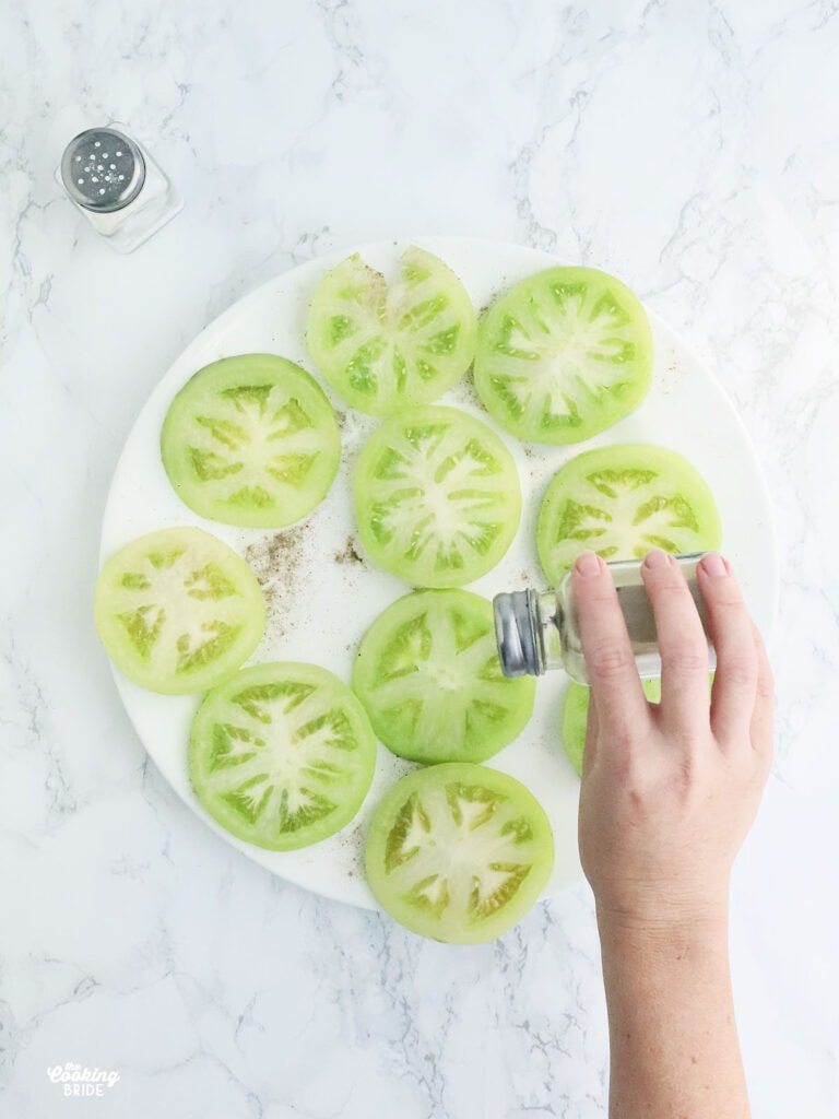hand seasoning sliced green tomatoes with salt and pepper