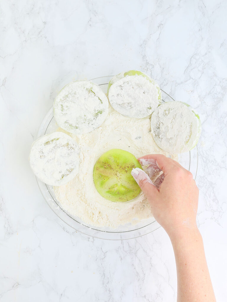 hand coating a sliced green tomato in flour
