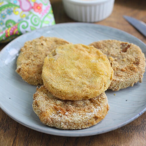 Four fried green tomatoes on a grey plate with a platter of fried green tomatoes in the background.