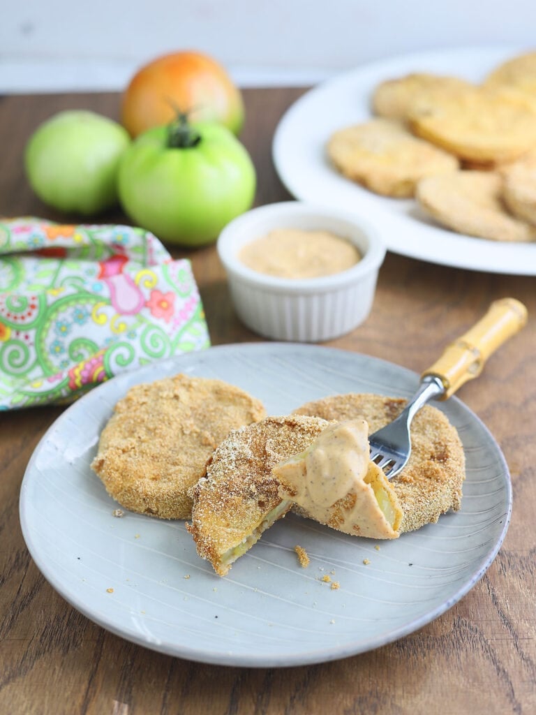 Fork with a slice of fried green tomatoes covered in dipping sauce on a grey plate.