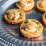 close up shot of shrimp on fried grit cakes garnished with green onions on a pewter platter