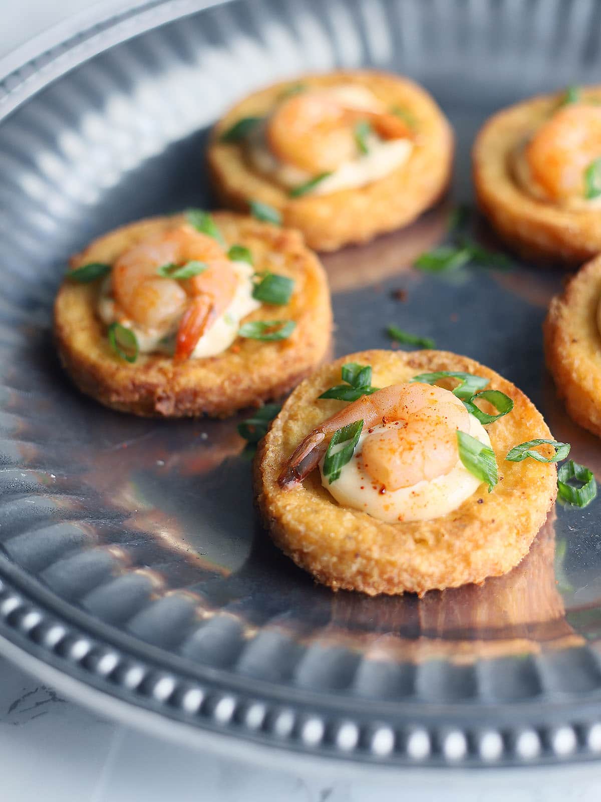 close up shot of shrimp on fried grit cakes garnished with green onions on a pewter platter