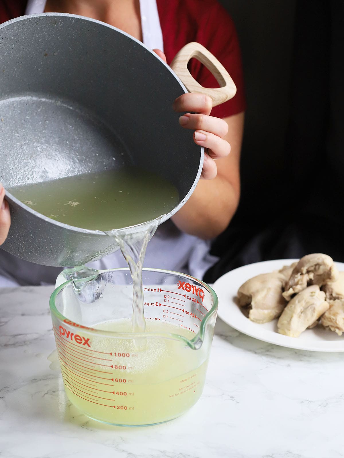 figure pouring off chicken broth into a glass measuring cup