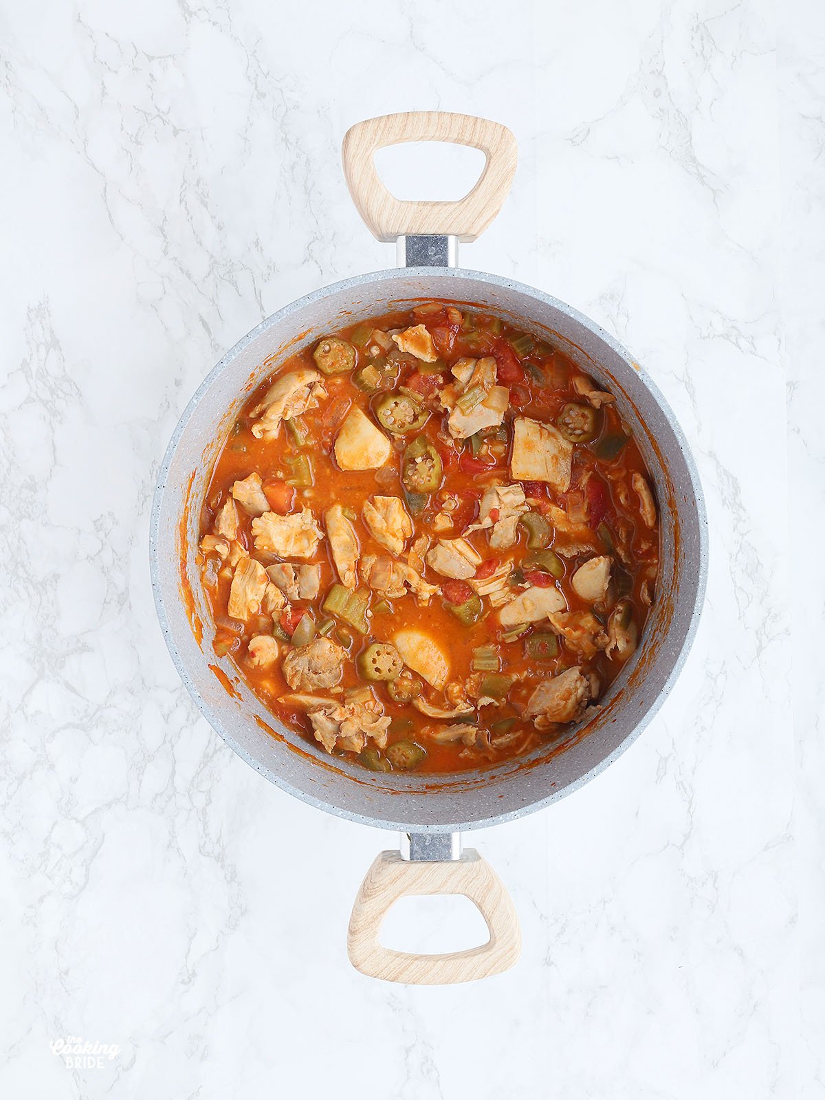 overhead shot of a gray pot of chicken peanut stew on a white marble background