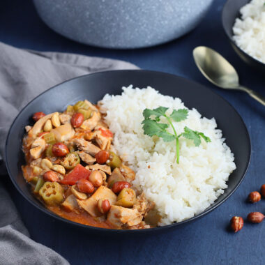 black bowl filled with rice and chicken peanut stew with a gold spoon to the side