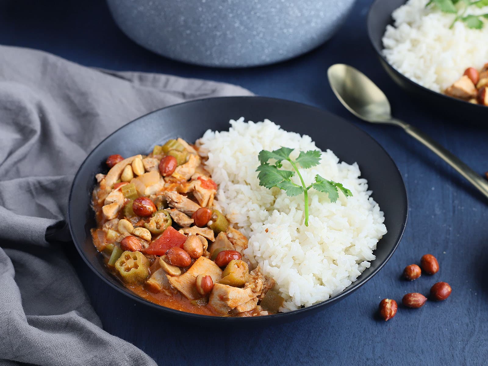 black bowl filled with rice and chicken peanut stew with a gold spoon to the side