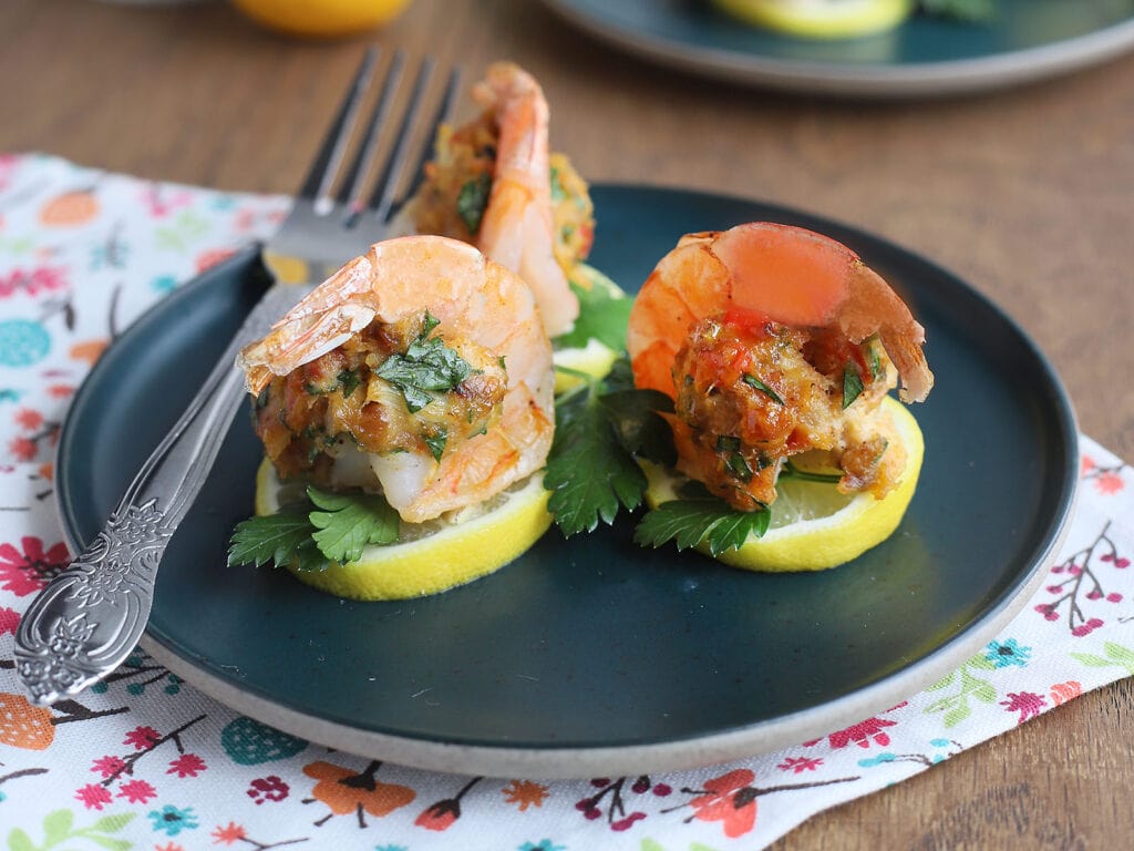 Three crab stuffed shrimp and a fork on a teal plate.