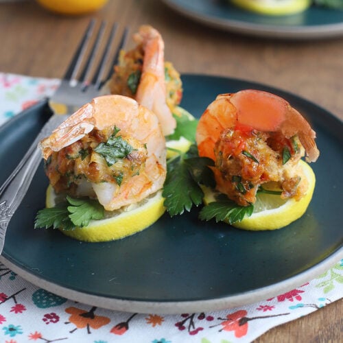 Three crab stuffed shrimp and a fork on a teal plate.