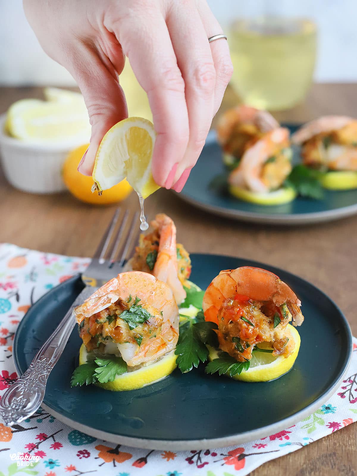 hand squeezing lemon juice over crab stuffed shrimp on a teal colored plate