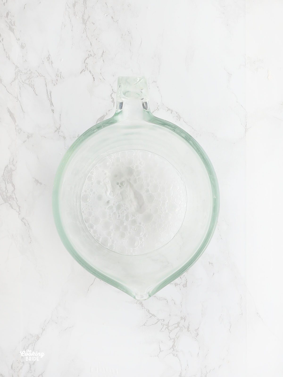 overhead shot of baking soda and vinegar fizzing up in a glass measuring cup