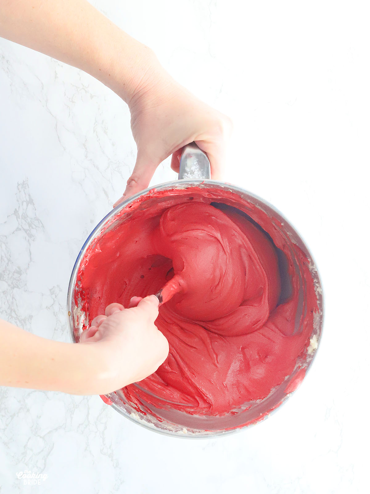 overhead shot of hands folding baking soda and vinegar together in a metal mixing bowl