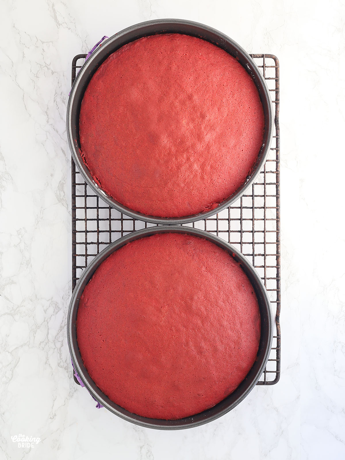 red velvet cake layers cooling in round cake pans on a wire rack