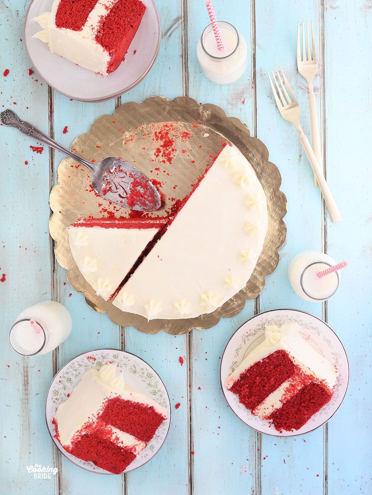 overhead shot of sliced red velvet cake with two slices of cake on plates and bottles of milk to the side