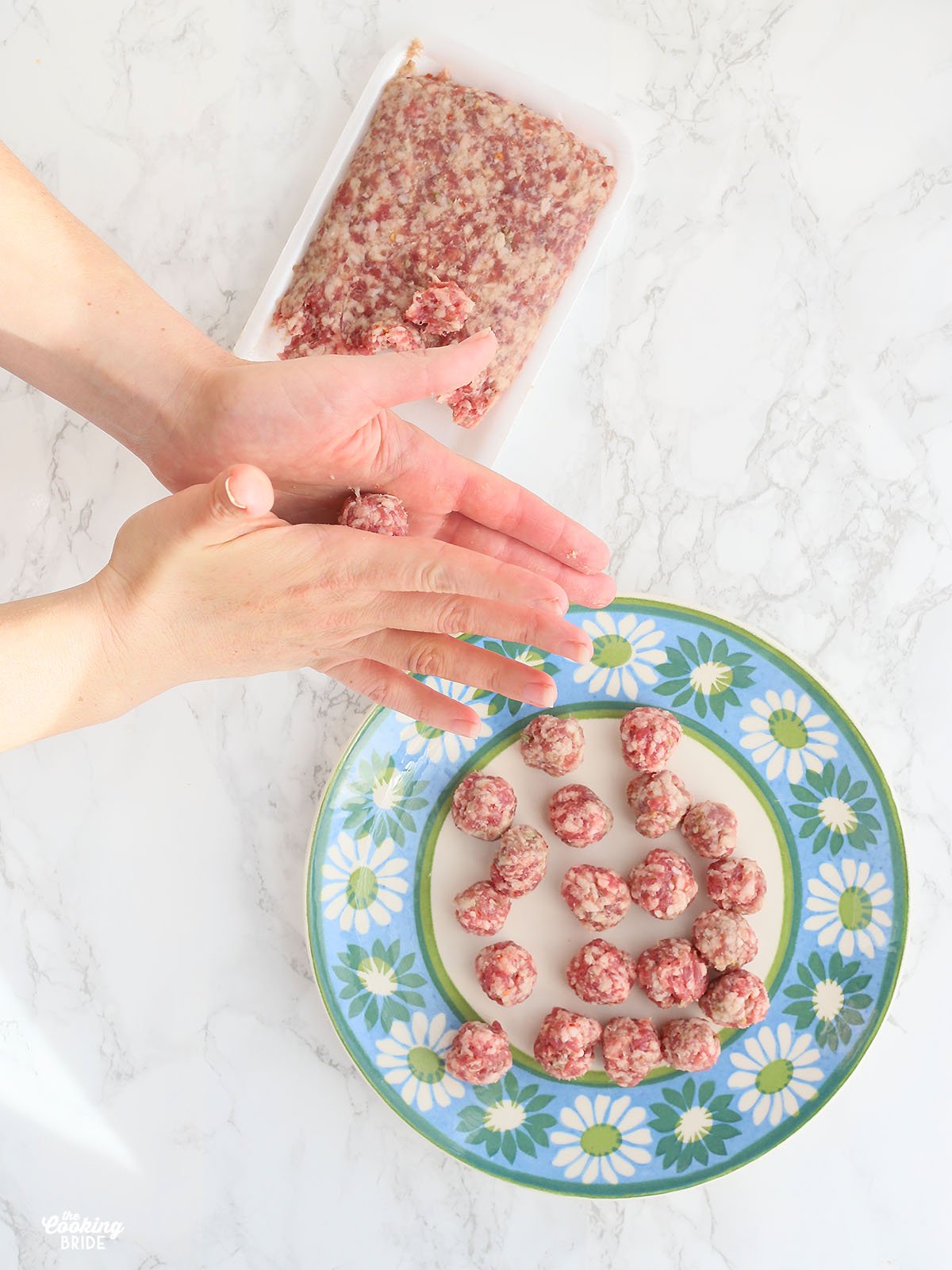 Hands rolling Italian sausage into meatballs.