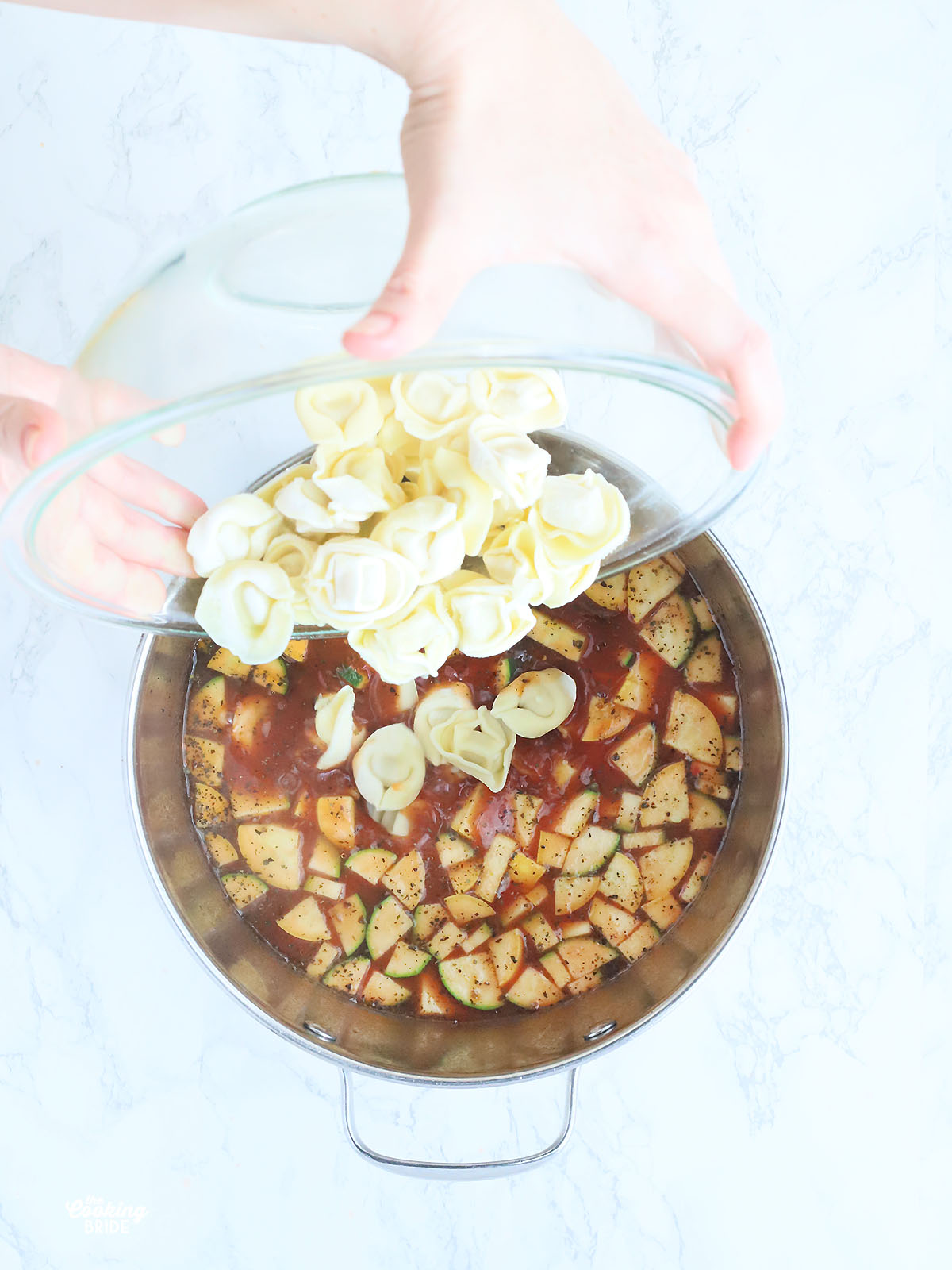 Hands pouring frozen tortellini into a pot of meatball tortellini soup.