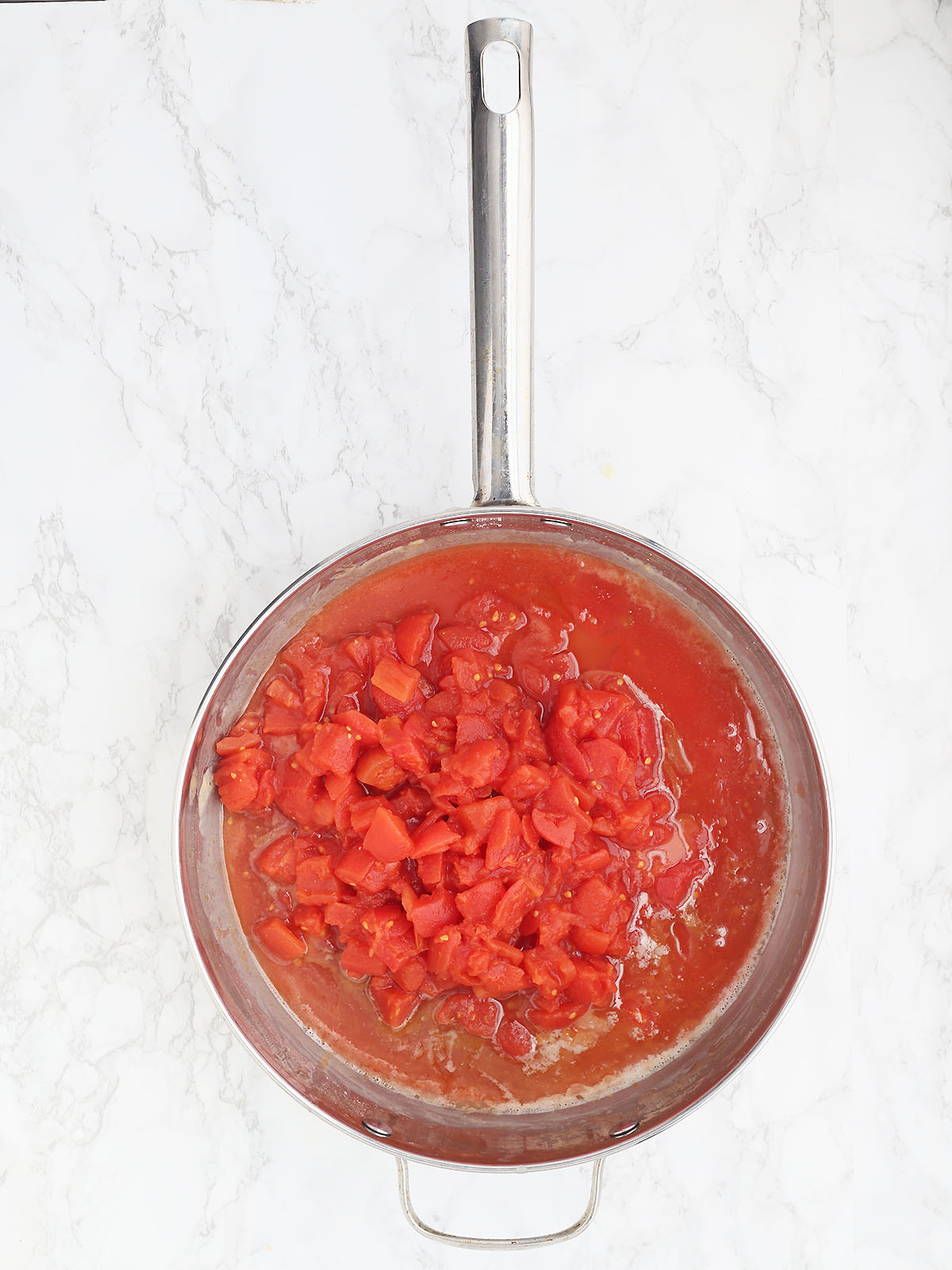 overhead shot of a stainless steel pan with diced tomatoes before being stirred into the rouxe