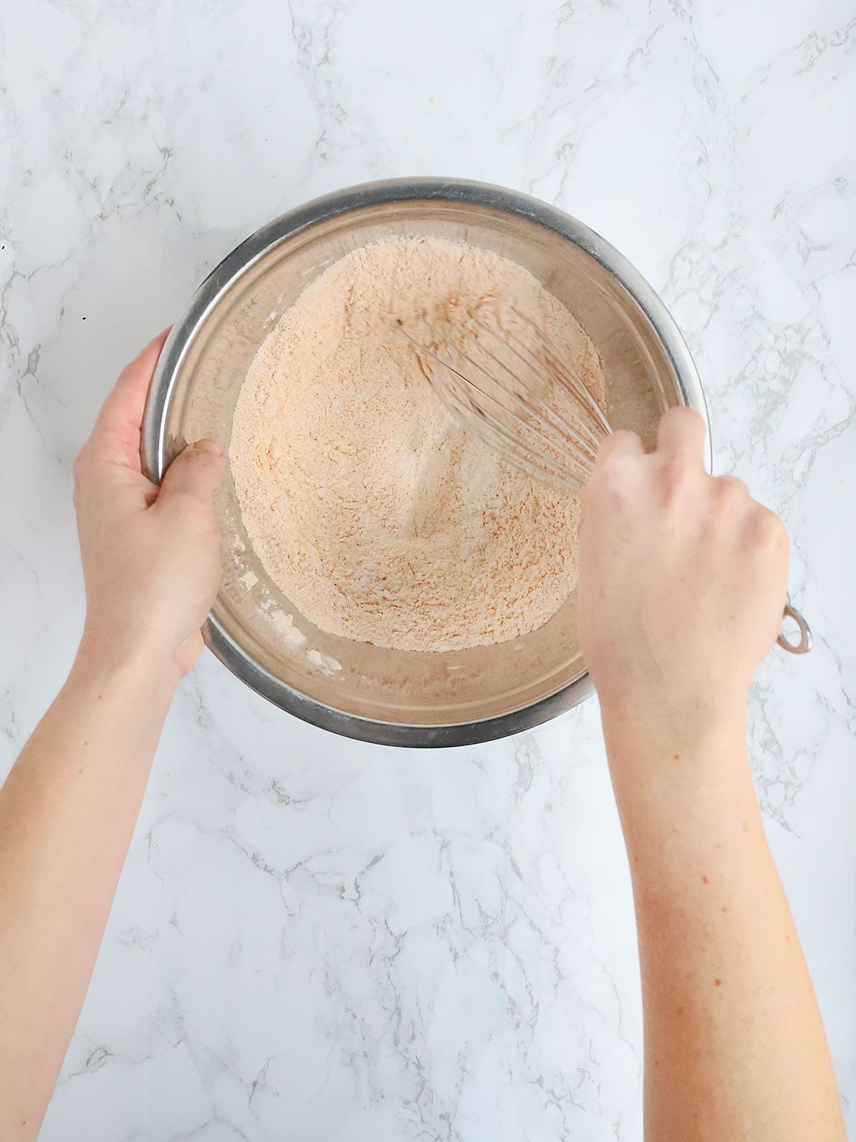 hands whisking together flour an seasoned salt in a metal mixing bowl