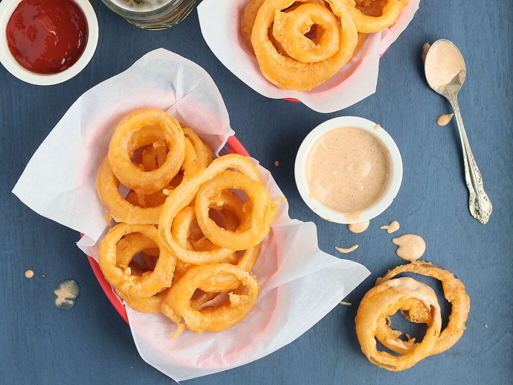 overhead shot of beer battered onion rings in two paper lined red baskets
